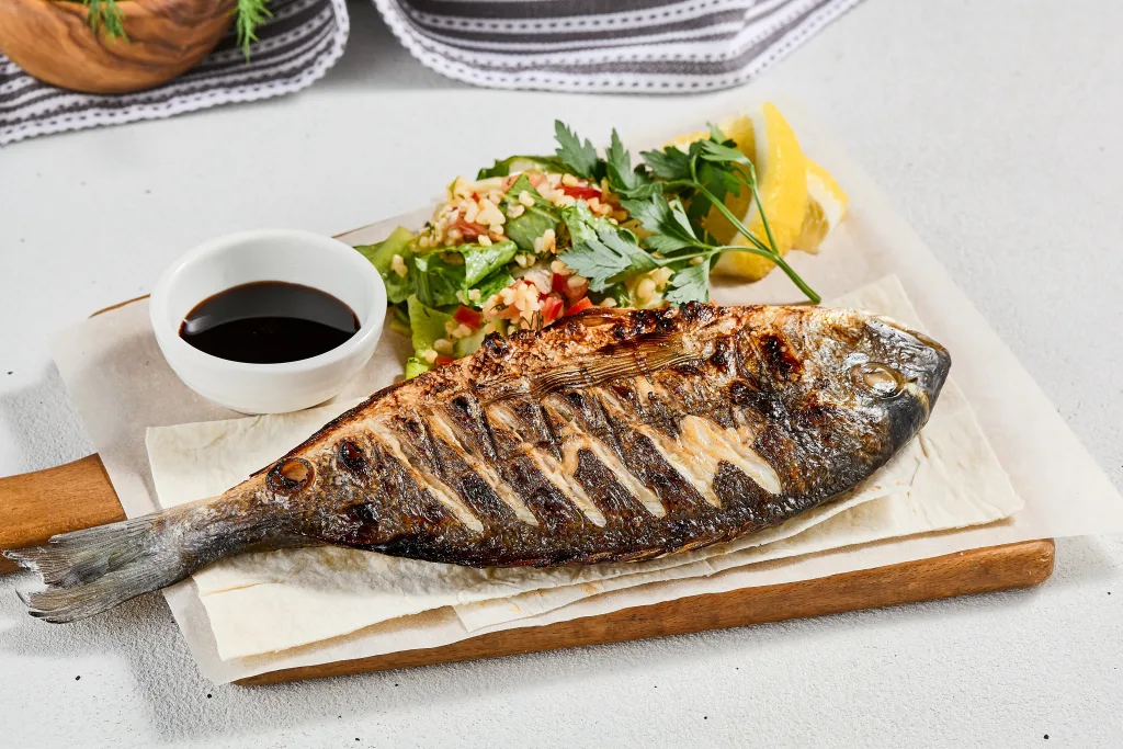 Grilled fish with garnish on concrete background